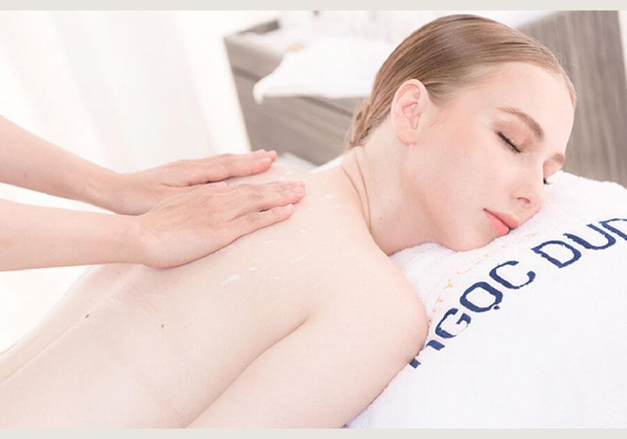 Người đang nằm thư giãn trên giường massage, được mát-xa lưng, trong không gian spa.
