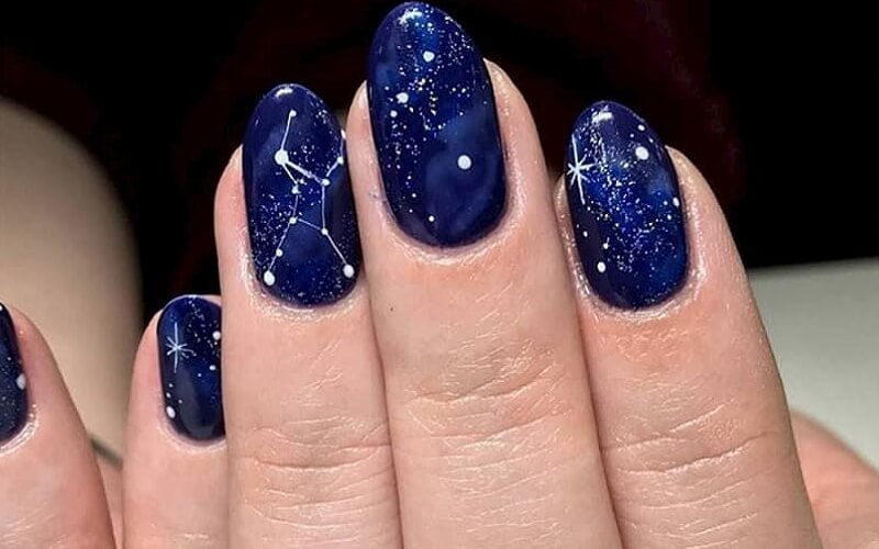 Top 15+ Mẫu Sơn Đầu Móng Kim Tuyến Đẹp Sang Trọng, Cuốn Hút 7 Móng tay được sơn màu xanh đậm, trang trí họa tiết chòm sao và điểm sáng như bầu trời đêm.