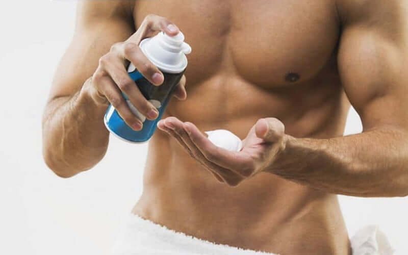 Người đàn ông cầm chai xịt tạo bọt và đang xịt vào tay, phía sau là nền trắng.
