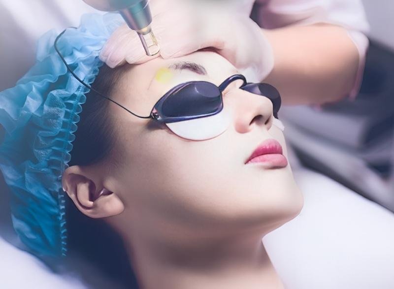 Người phụ nữ đeo kính bảo hộ đang được thực hiện liệu trình chăm sóc da bằng thiết bị chuyên dụng.