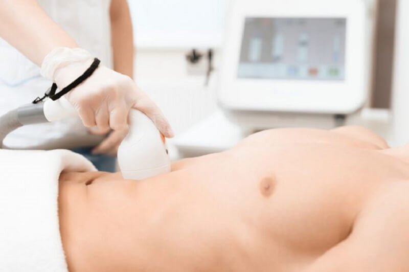 Nhân viên y tế đang sử dụng thiết bị chăm sóc da trên bụng của một người trong phòng khám.