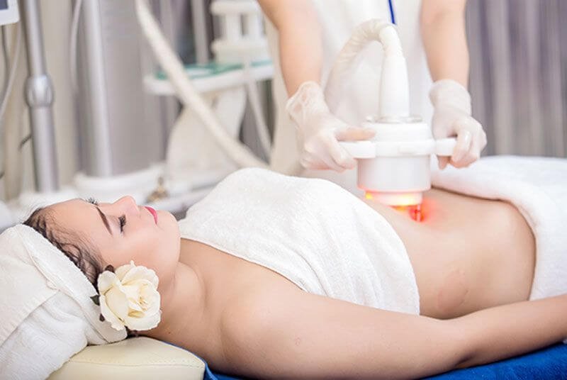 Người nằm thư giãn trên giường spa trong khi thực hiện liệu pháp chăm sóc cơ thể bằng máy móc hiện đại.