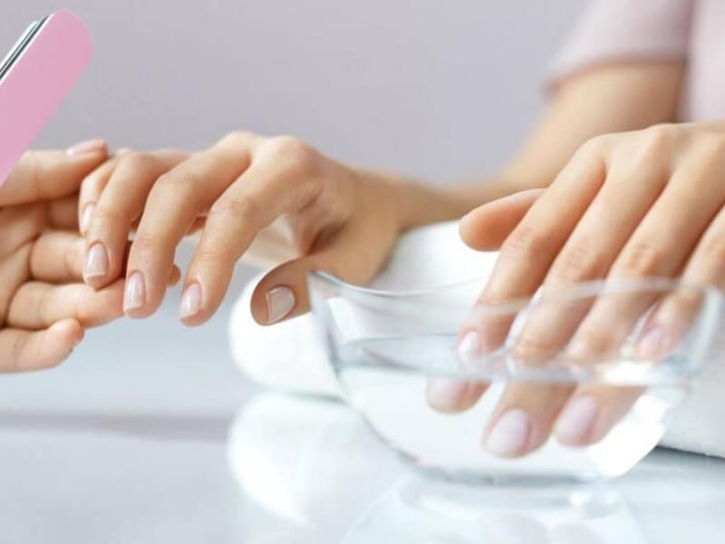 Người đang làm móng tay, sử dụng dũa và bát nước, trong không gian sáng sủa và sạch sẽ.