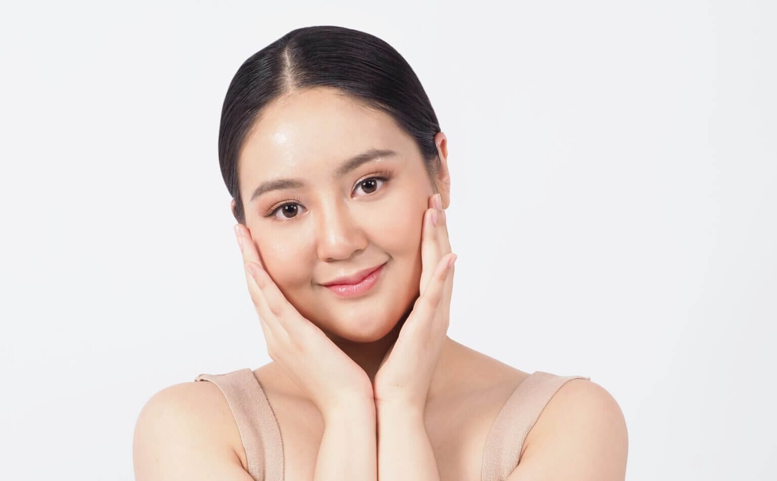 Người phụ nữ trẻ mỉm cười, hai tay nâng nhẹ khuôn mặt, nền trắng.