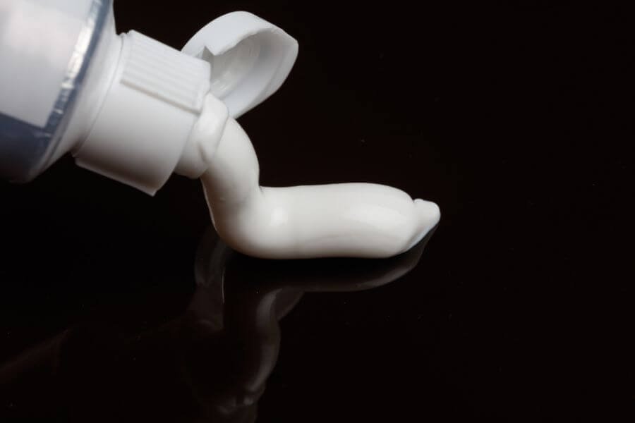Ống kem đang được bóp, kem trắng chảy ra trên nền đen.