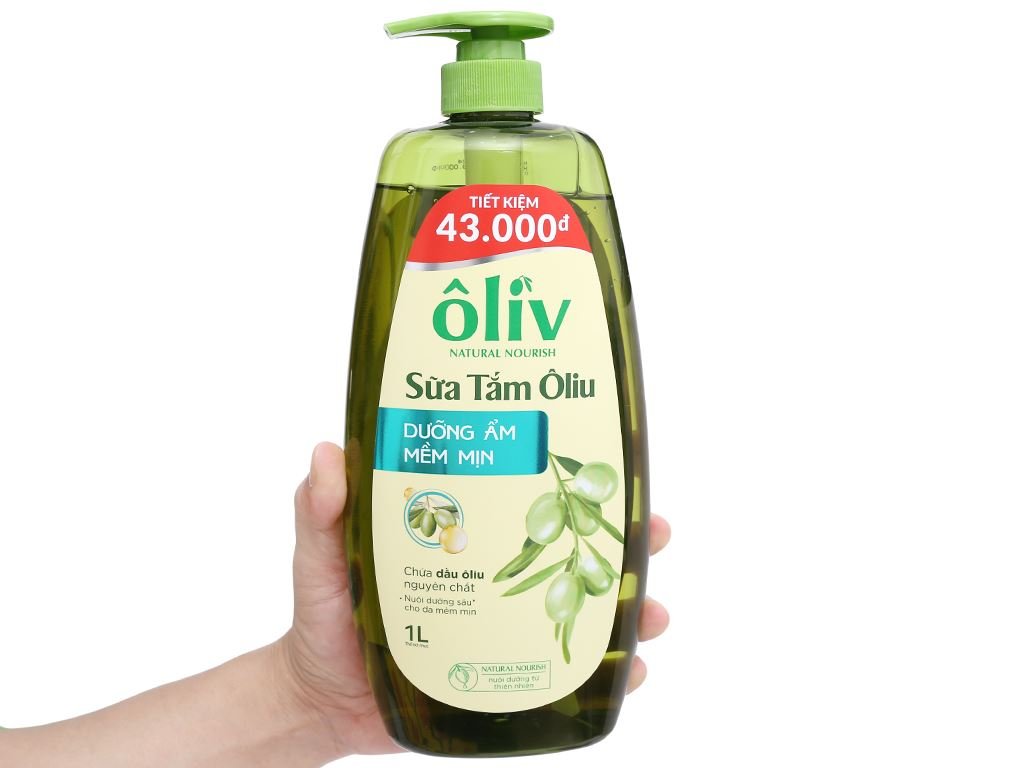 Chai sữa tắm ô liu 1L màu xanh lục, có nắp bơm, được cầm trên tay, nổi bật thông tin dưỡng ẩm mềm mịn.