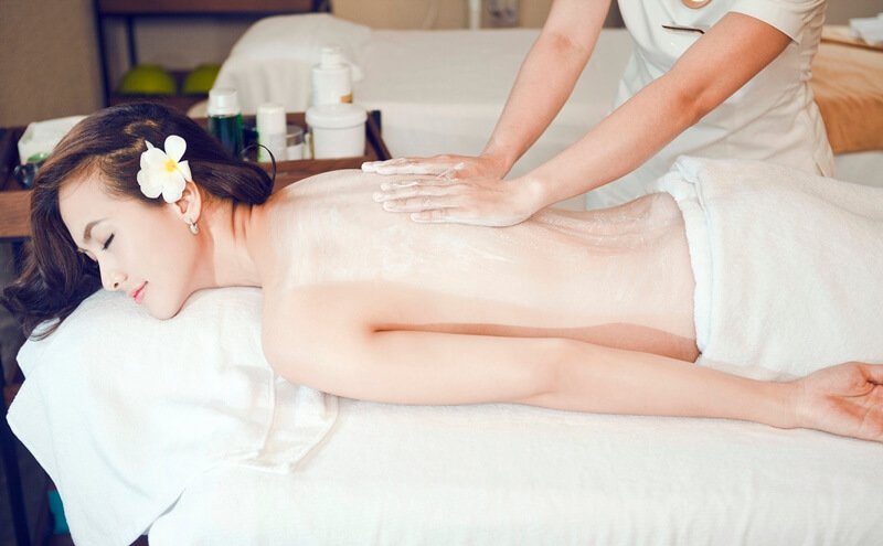 Người đang được massage thư giãn trên giường spa, có khăn phủ và hoa cài trên tóc.