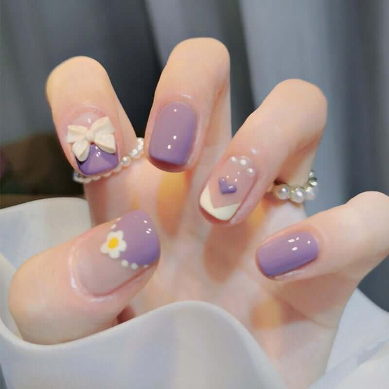 Bàn tay với móng tay được sơn màu tím trang trí hoa, nơ và họa tiết trái tim.