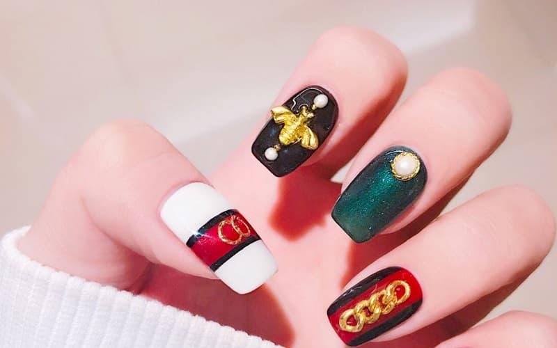 Bàn tay với móng tay được trang trí bằng họa tiết và màu sắc nổi bật, gồm đen, trắng, đỏ, và xanh lục.