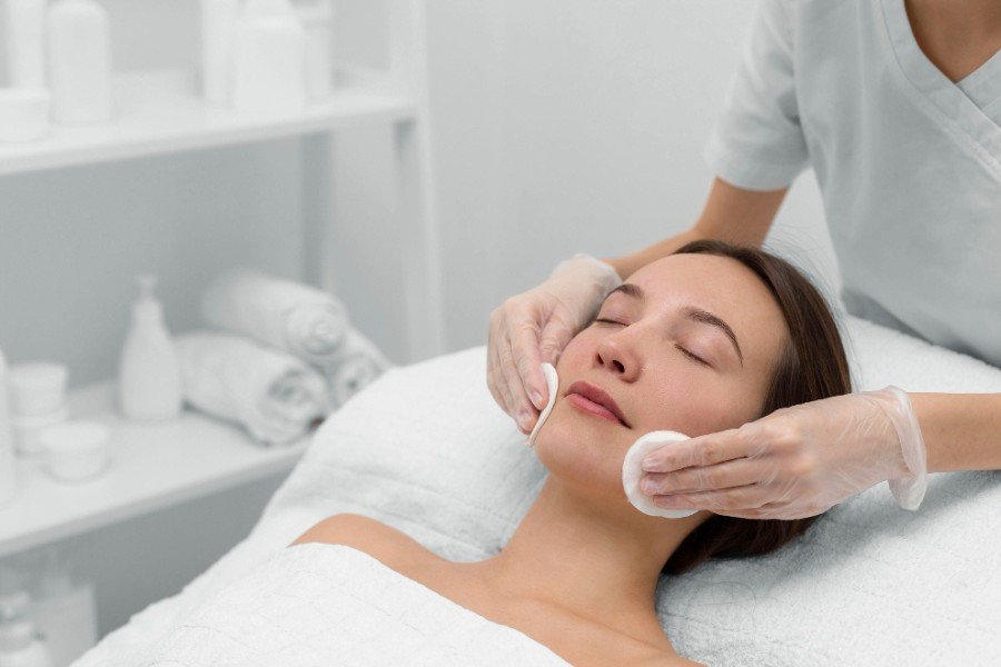 Người phụ nữ nằm thư giãn trong spa, được chăm sóc da mặt bởi chuyên viên đeo găng tay.