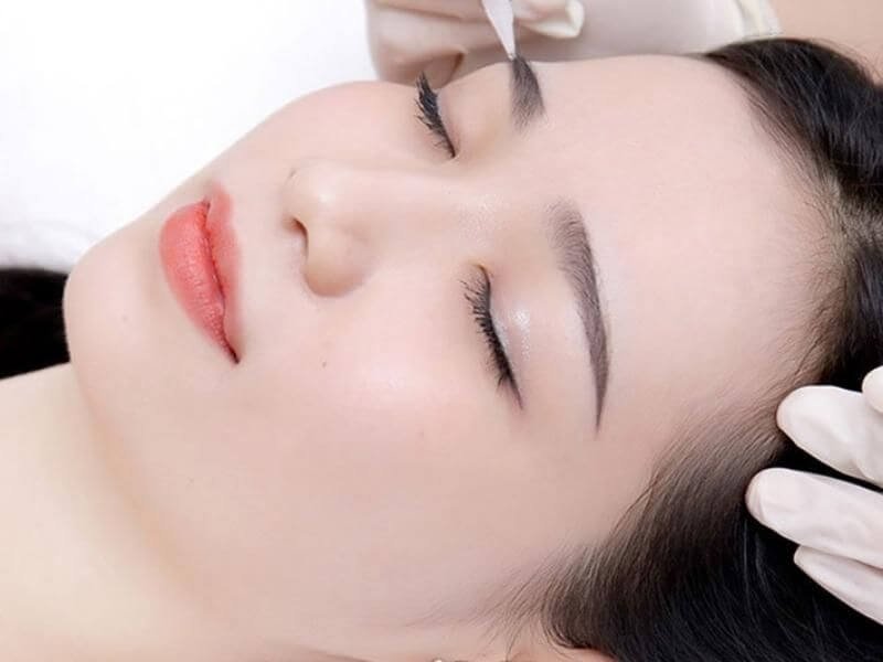 Người đang nhắm mắt thư giãn, được chăm sóc da mặt bởi một người đeo găng tay trắng.