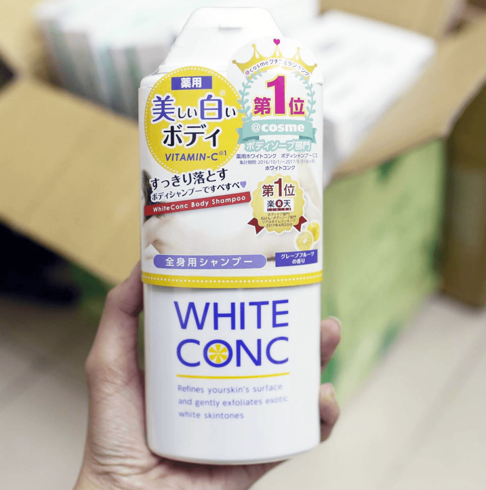 Người cầm chai sữa tắm White Conc, bao bì có chữ tiếng Nhật và hình ảnh trái cây màu vàng.